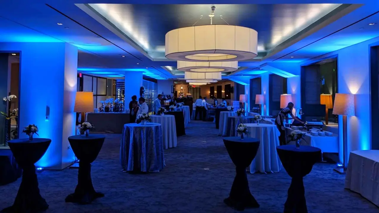 A hotel ballroom with tall tables, lit with blue uplighting along the walls