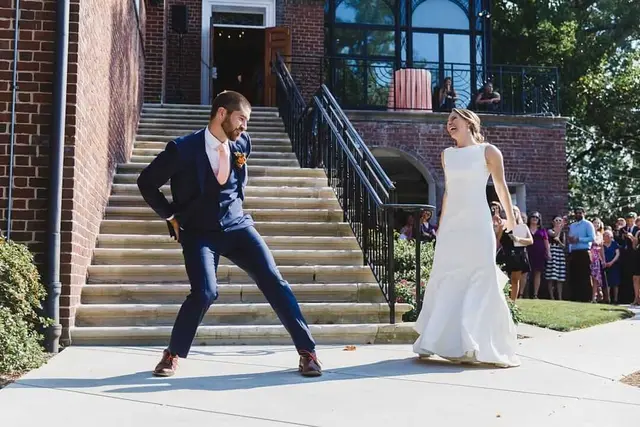A bride and groom dance on a brick staircase outside their venue while guests watch