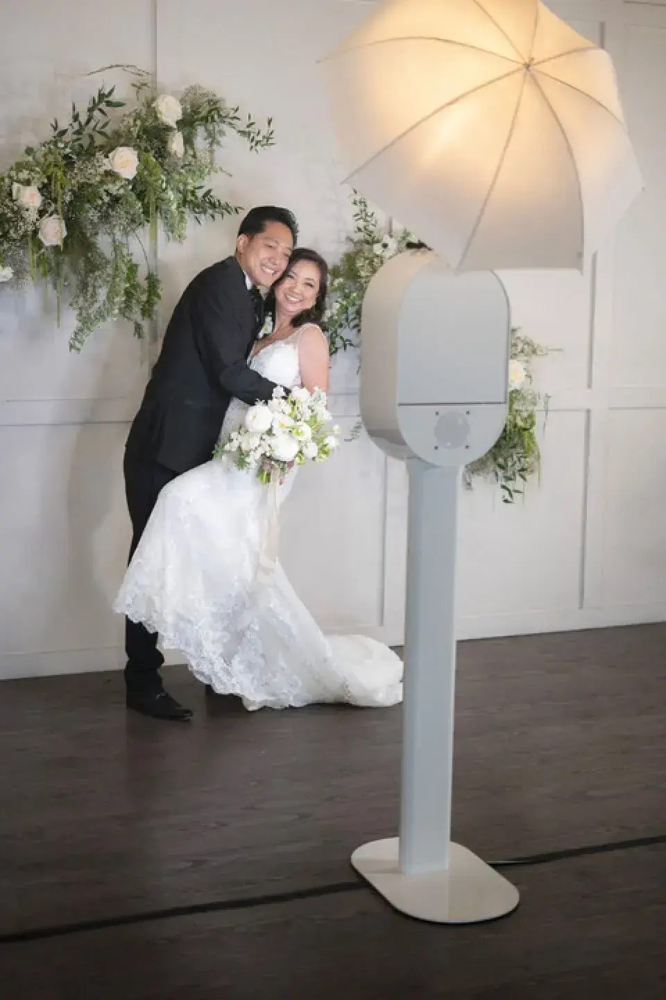 A bride and groom pose in front of a white digital photo booth