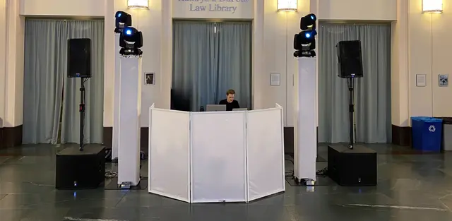 A white DJ booth flanked by speakers and two moving-head lights on stands